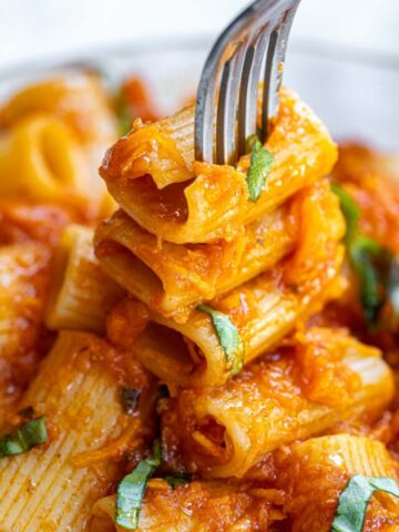 Close-up of rigatoni pasta covered in tomato sauce, garnished with freshly chopped basil, with a fork piercing some pieces. vibrant and appetizing.