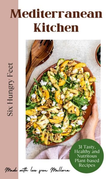 A cookbook titled "Mediterranean Kitchen" by Six Hungry Feet, featuring a wooden spoon and a large bowl of mixed salad with zucchini, greens, feta cheese, and nuts. The cover notes "31 Tasty, Healthy and Nutritious Plant-based Recipes" and "Made with love from Mallorca.