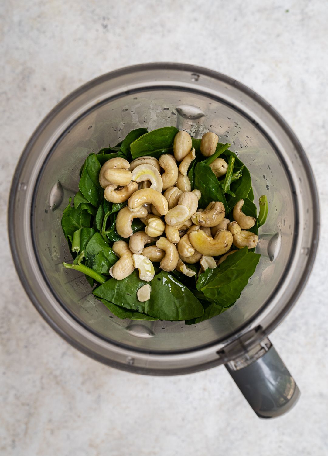 Blending cashews, spinach, and olive oil to make a green sauce.