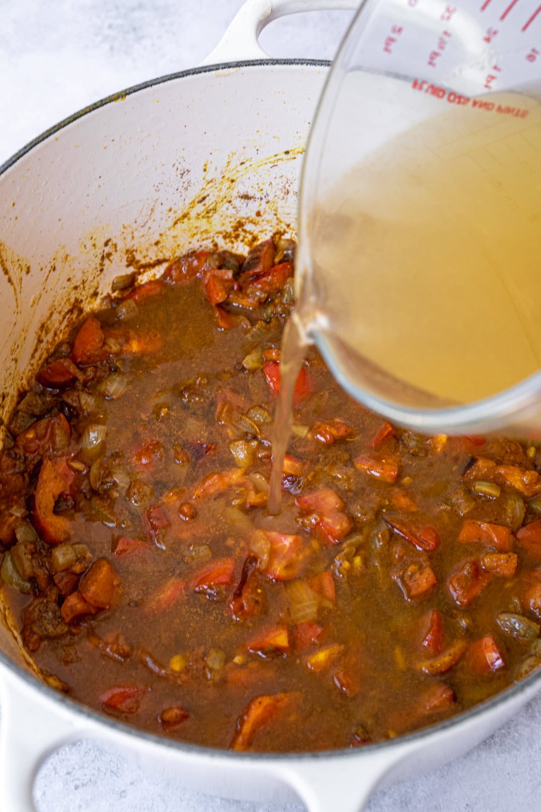 Adding fresh tomato and vegetable stock to the pot.