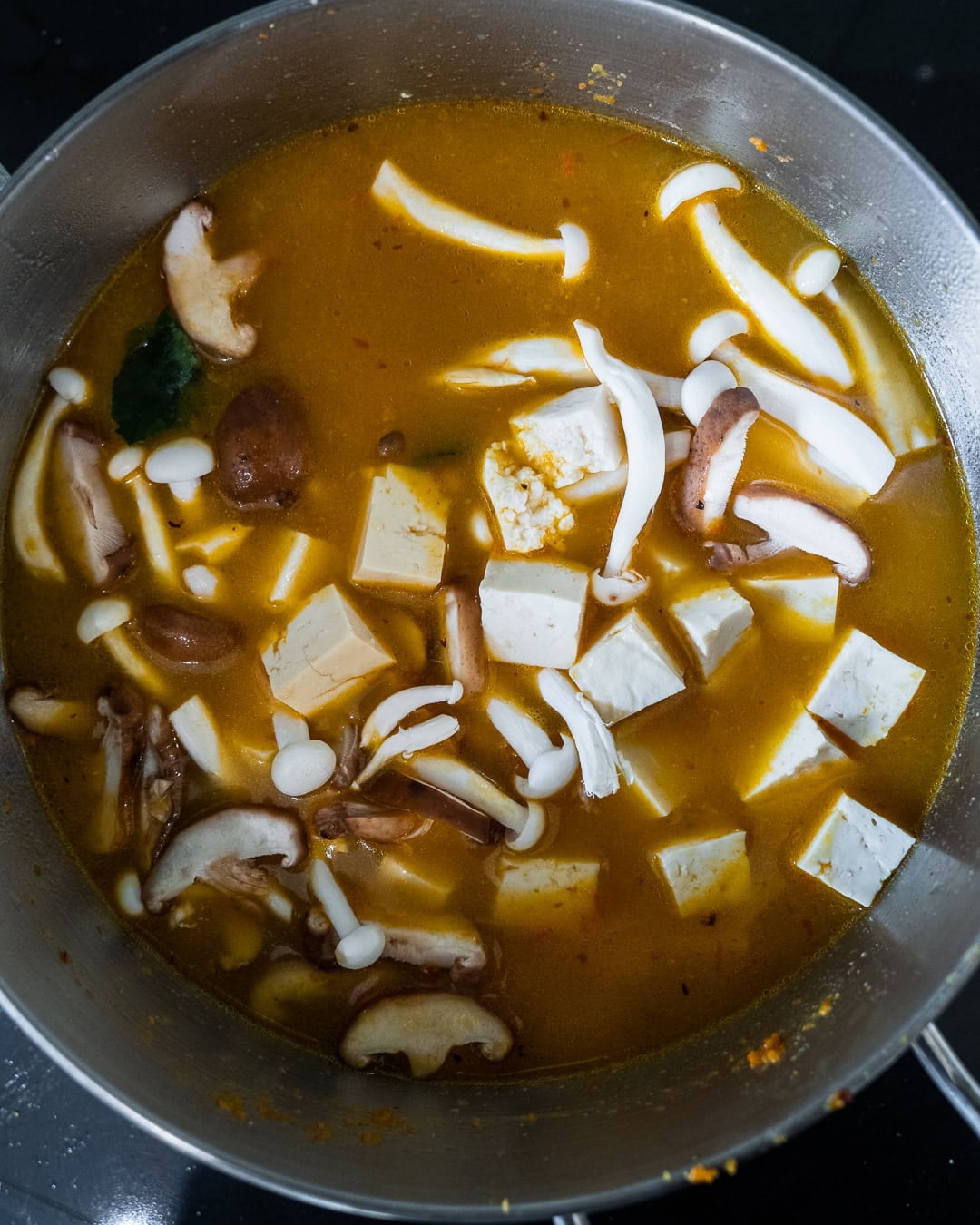 Adding vegetable stock, mushrooms, and tofu