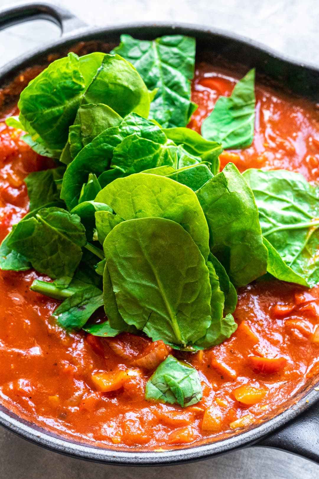Adding fresh spinach to the shakshuka