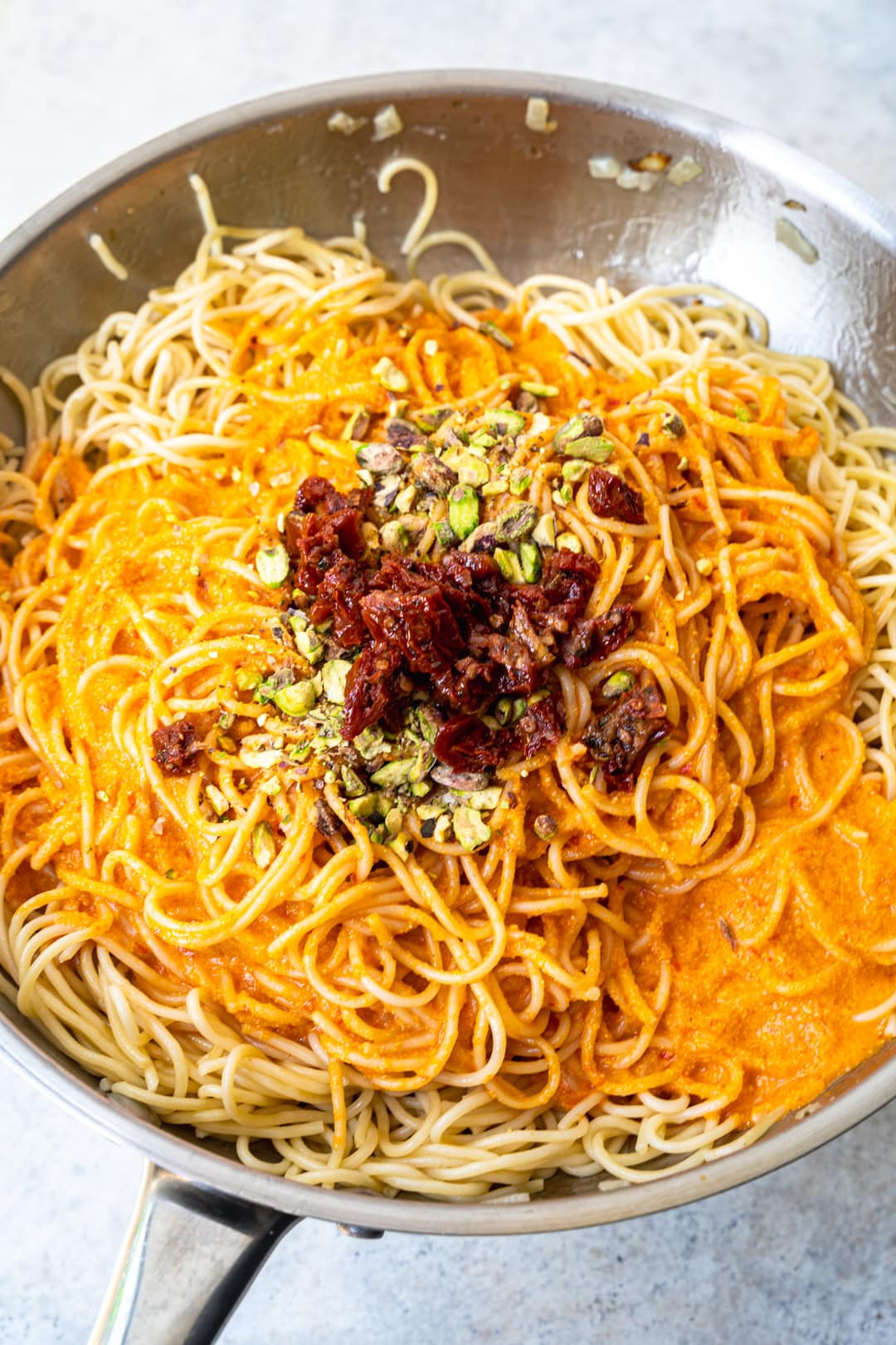 Combining the pasta with the harissa sauce and toppings.