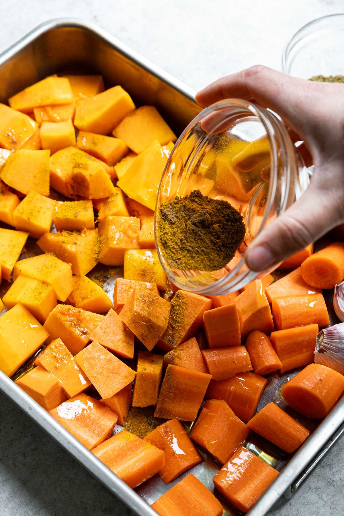 Adding olive oil and spices to the vegetables on the tray